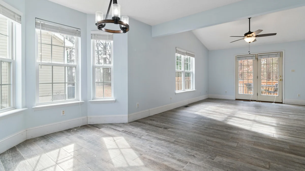 Sala de estar clara e vazia com piso e ventilador de teto em madeira, ideal para uso em design de interiores.