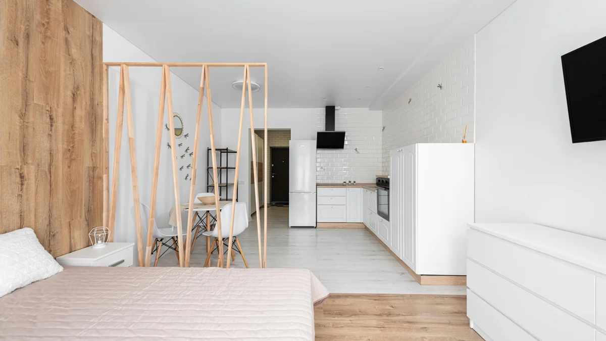 Quarto com design criativo, cama, TV e refrigerador com armários no chão, em ambiente claro.