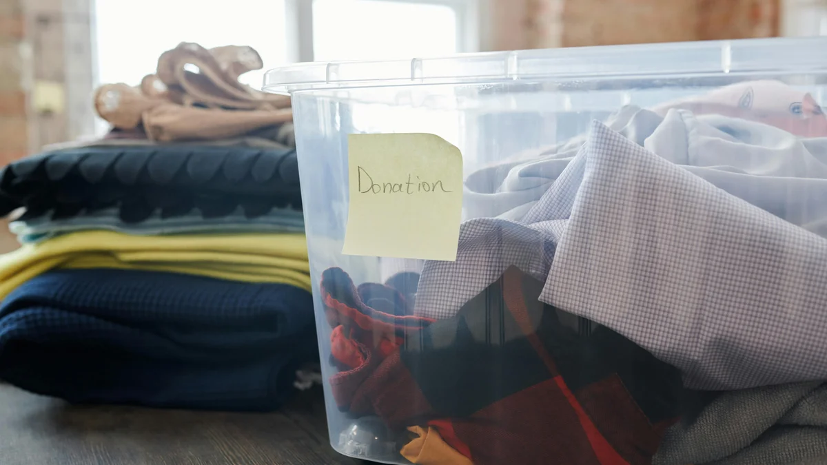 Caixa plástica transparente cheia de roupas etiquetadas 'Doação' para uma campanha de caridade.