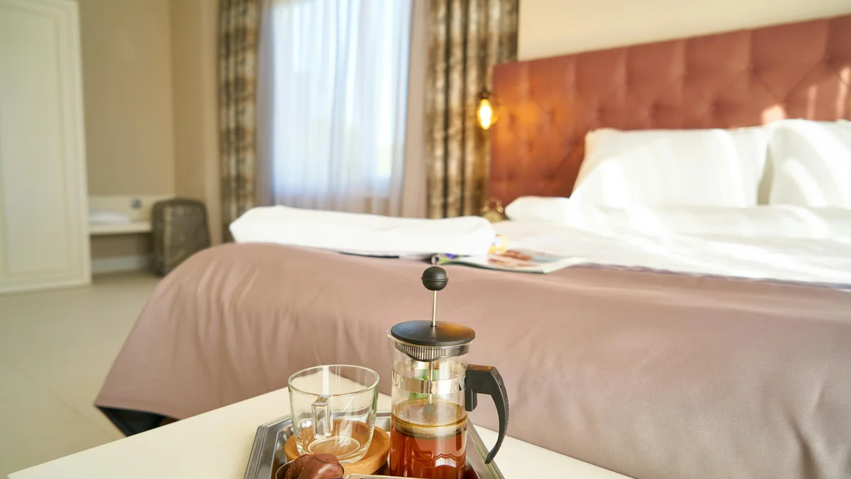 Quarto de hotel convidativo com uma prensa francesa para café na mesa de cabeceira, ideal para relaxamento e viagens.