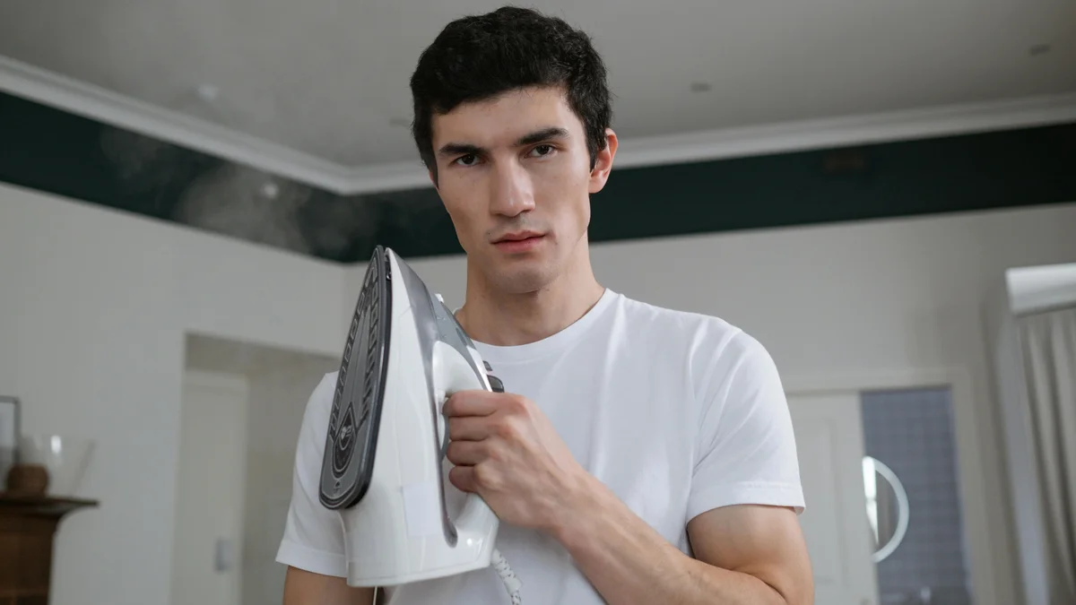 Um homem jovem segura um ferro a vapor em uma sala de estar moderna, preparando-se para as tarefas de casa.