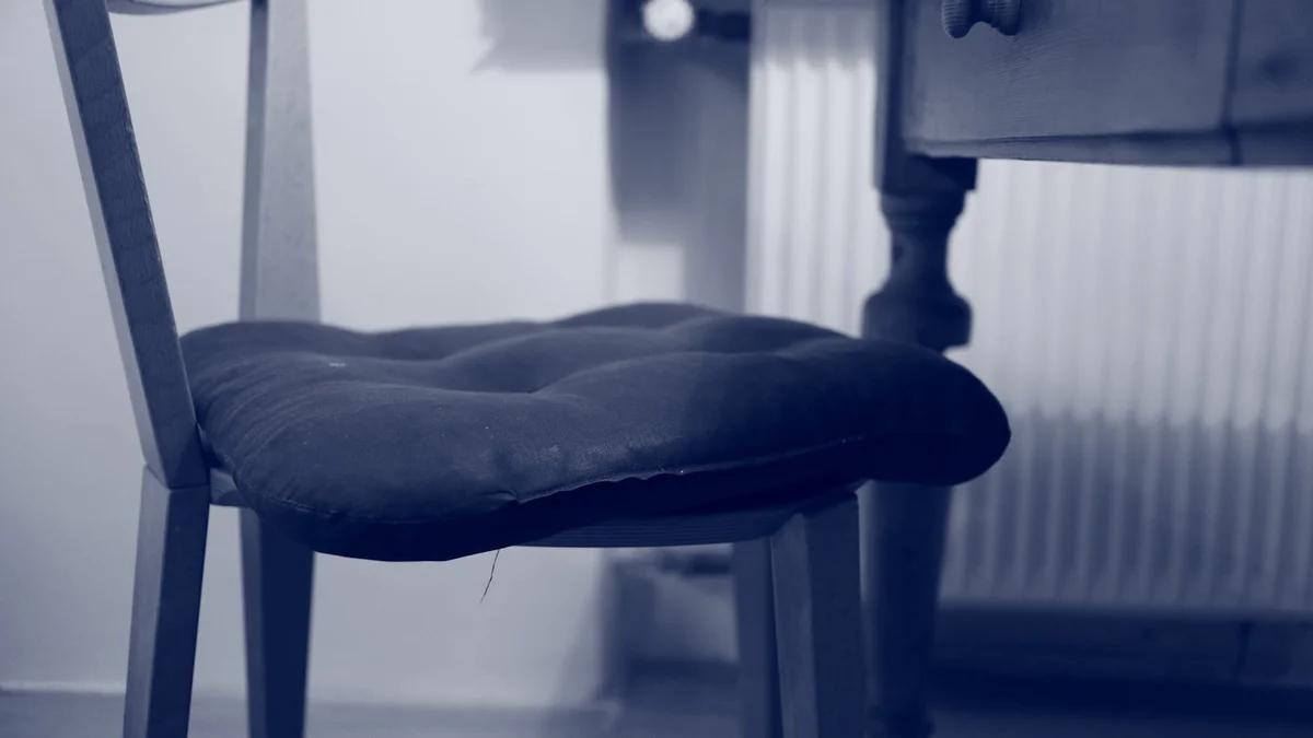 Cadeira de madeira com almofada de assento capitonê, posicionada próxima a uma escrivaninha, sugerindo um espaço de estudo ou trabalho funcional.