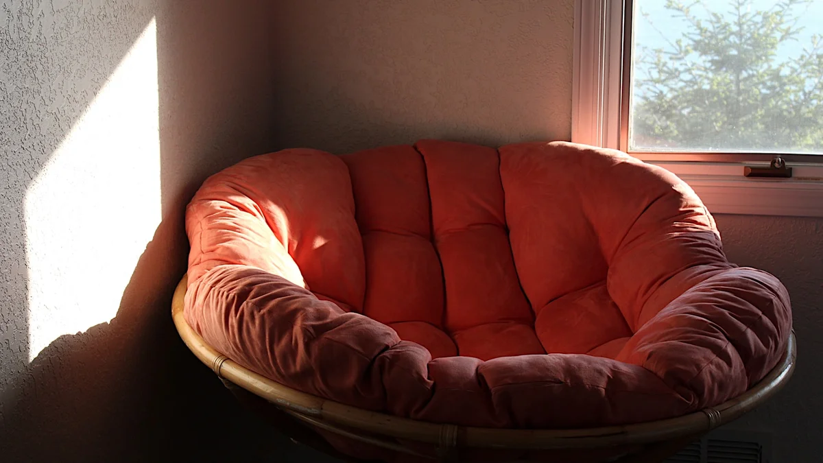 Poltrona confortável posicionada em frente a uma janela em um quarto, recebendo luz natural e criando um ambiente relaxante.