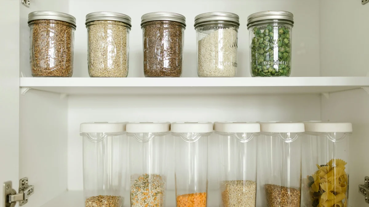Despensa organizada com grãos em potes de vidro e alimentos secos em recipientes plásticos.