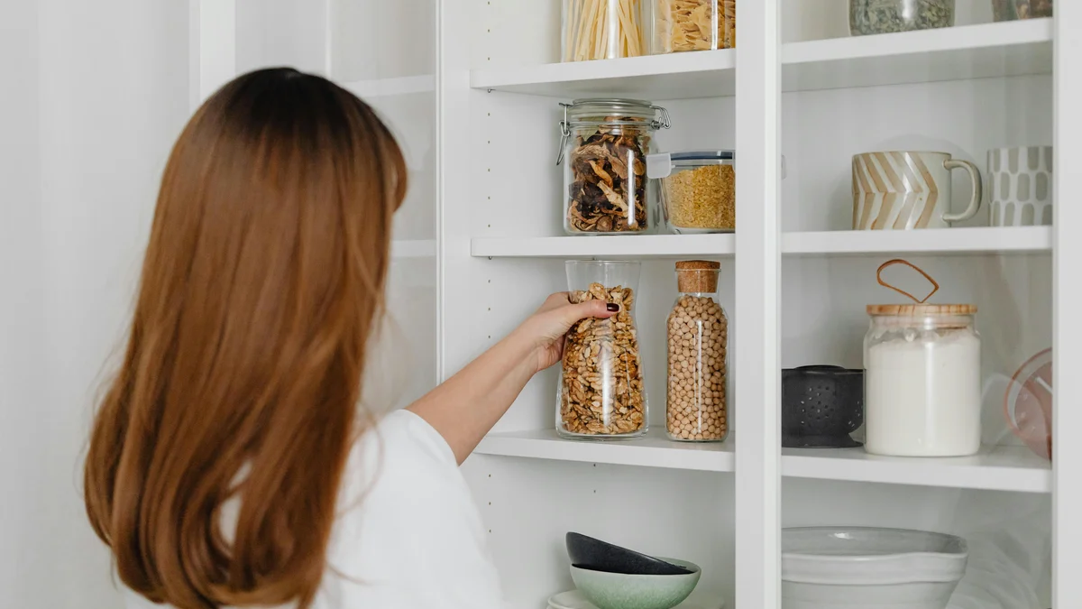 Mulher organizando potes em prateleiras de despensa para armazenamento de alimentos.