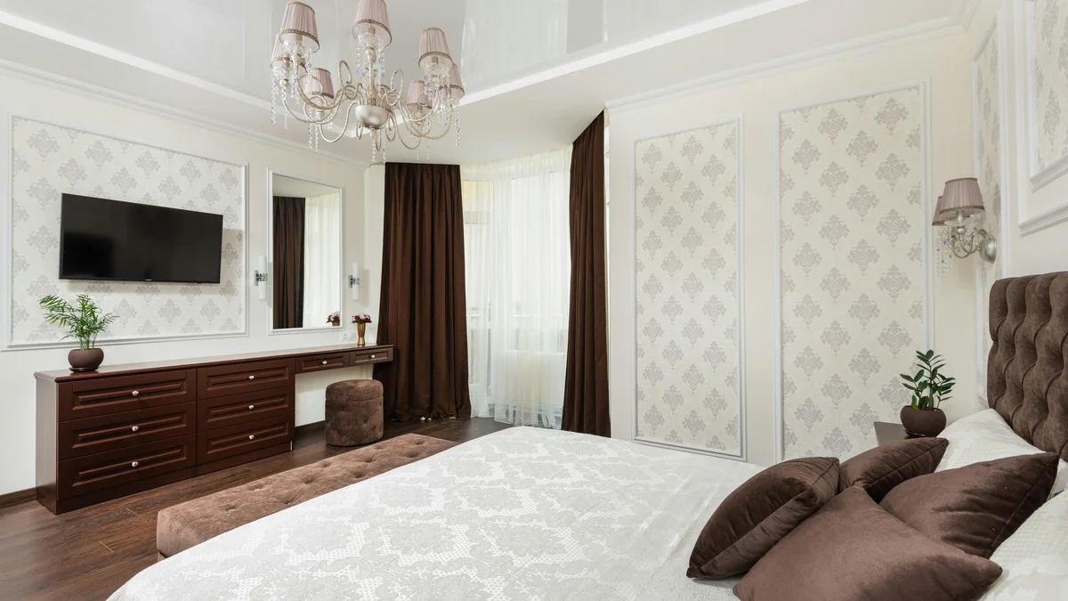 Quarto espaçoso com design luxuoso, apresentando almofadas macias, lustre e cômoda, evocando uma sensação de conforto e sofisticação.