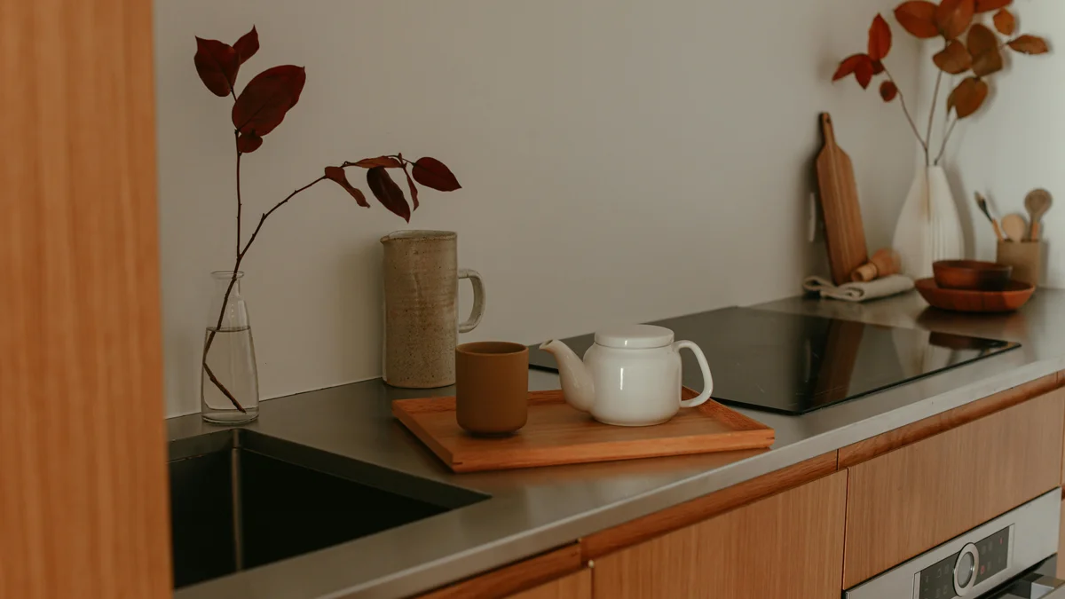 Bancada de cozinha minimalista com bule, caneca e decoração outonal em tons quentes.
