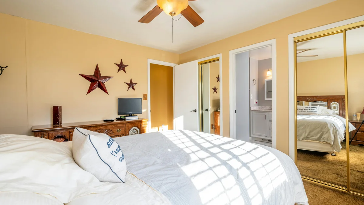 Quarto claro e ensolarado com decoração moderna e um ventilador de teto, ideal para um refúgio tranquilo e refrescante.