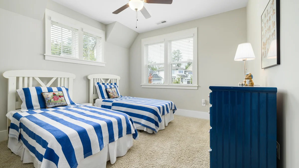 Quarto infantil claro e aconchegante com camas de solteiro, roupa de cama listrada azul e decoração elegante, com um ventilador de teto funcional.