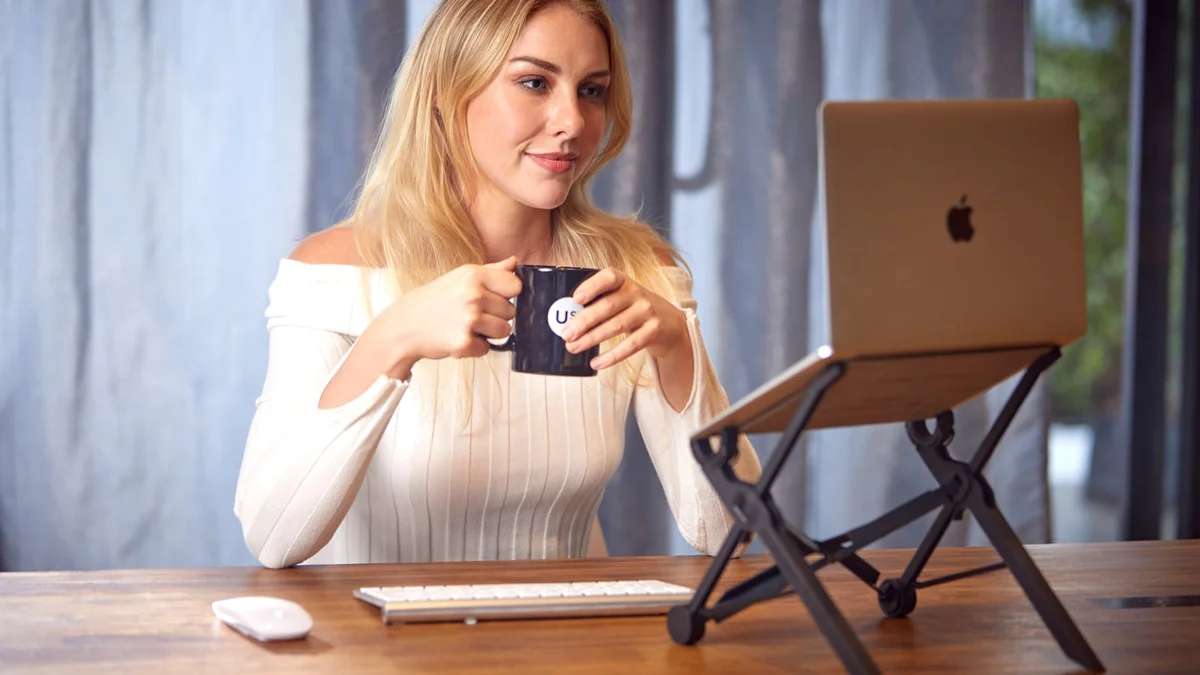 a woman sitting at a table with a laptop and a cup of coffee Ilustração editorial secção 2 sobre melhores suportes para