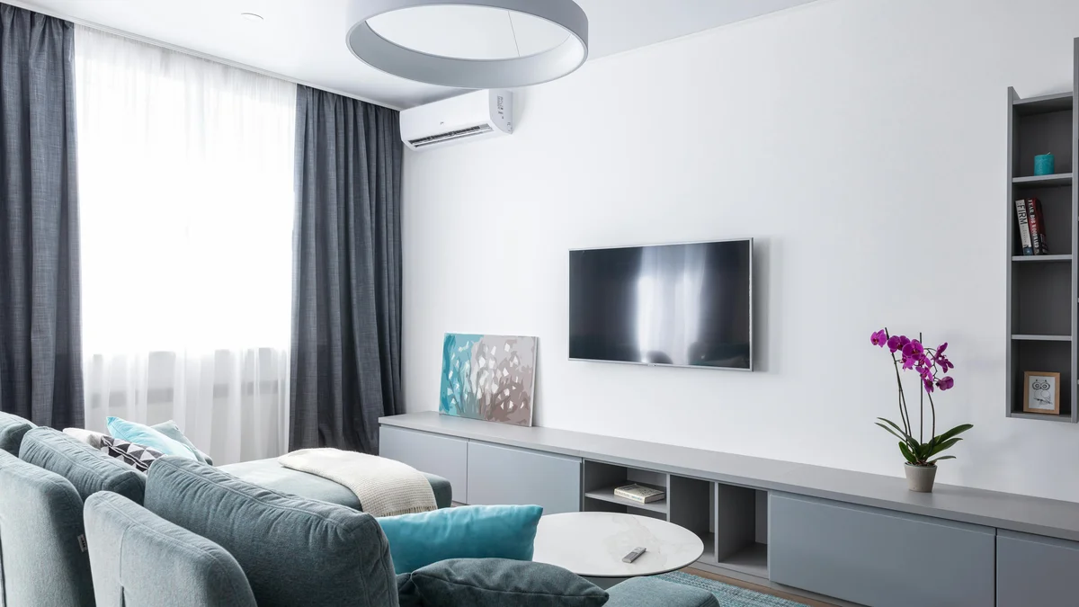 Interior moderno e aconchegante de sala de estar em tons de cinza, com TV na parede e um móvel cinza com orquídea florida.