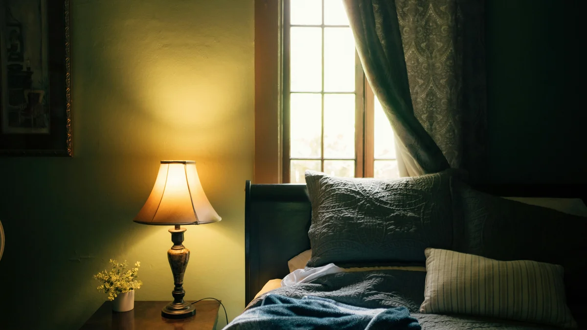 Quarto com iluminação suave, cama com travesseiros macios e cortinas elegantes próximas à janela.