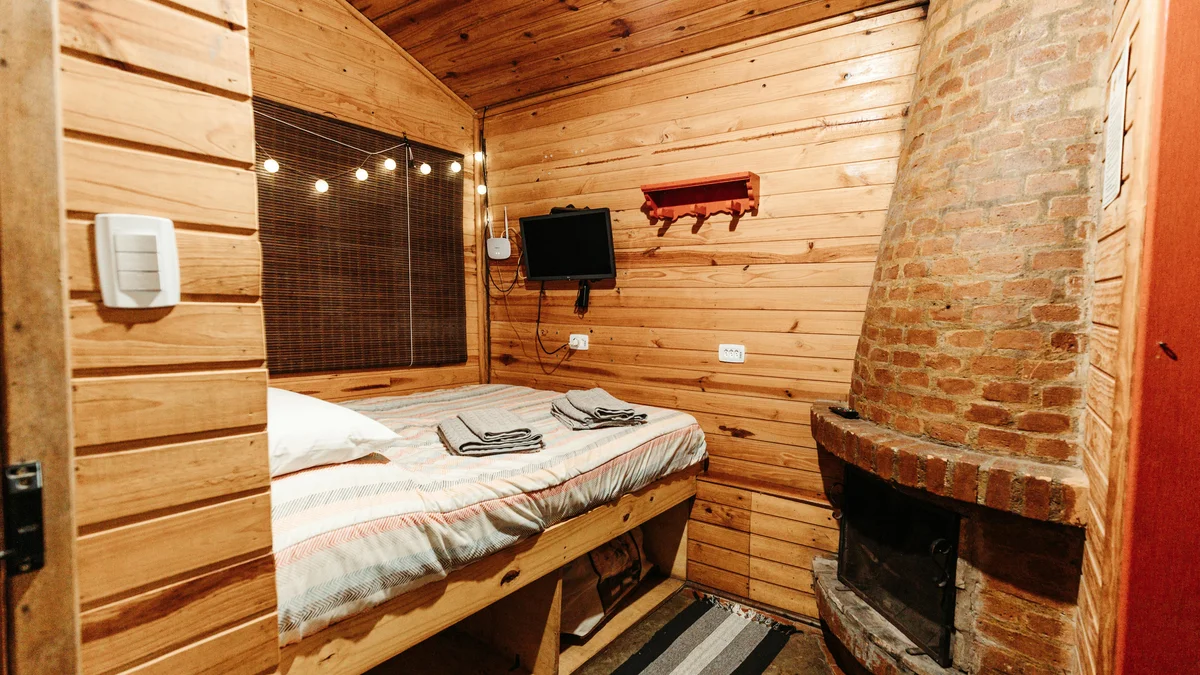 Quarto rústico em cabana de madeira com estrutura de cama e lareira de tijolos, proporcionando uma atmosfera aconchegante e charmosa.